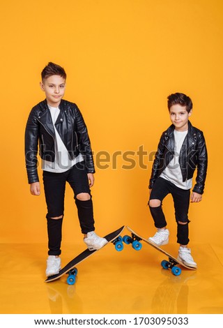 Little boys learning skateborading in studio yellow background. Cool happy teen friends brothers having fun, riding on skateboards and showing fashion popular movements