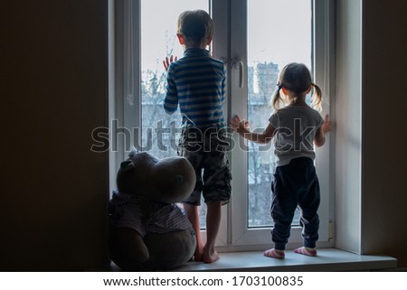 Stay at home. Quarantine coronavirus pandemic prevention. Boy and girl staying on windowsill and looks out window. Covid 19. Brother and sister look at the street and want to walking. Royalty-Free Stock Photo #1703100835