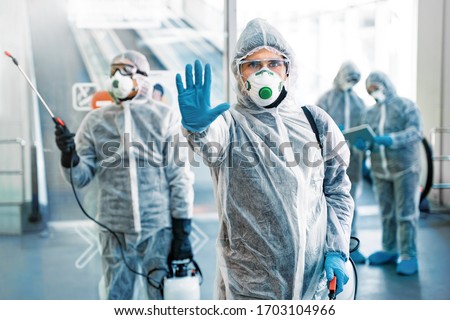 Healthcare worker showing stop gesture. Team of healthcare workers wearing hazmat suits working together in shopping centre, to control an outbreak of virus in the city Royalty-Free Stock Photo #1703104966