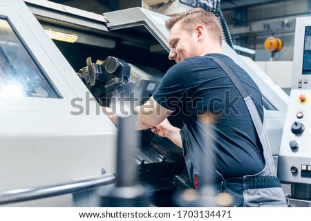 Experienced worker changing tool setup of lathe machine on the factory floor Royalty-Free Stock Photo #1703134471