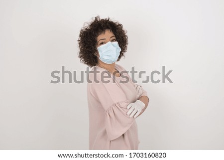 Pretty caucasian lady wearing face mask standing against gray wall with arms crossed wearing casual clothes. Looking and smiling at the camera. Confident successful woman.