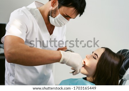 Closeup young woman at dentist clinic office. Male doctor performing extraction procedure with forceps removing patient tooth. Doctor in disposable medical facial mask. Royalty-Free Stock Photo #1703165449