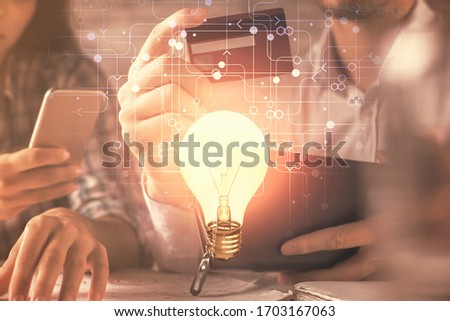 Double exposure of man and woman on-line shopping holding a credit card and light bulb hologram drawing. Idea concept.