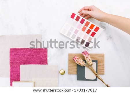 Interior designer selecting paint colors, fabric swatches, and remodel design samples. Overhead sample board lay down on white marble surface with pink color story
