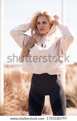 Beautiful young blonde woman in beige hoodie doing sport outdoor. Attractive female spending active time in the park. 