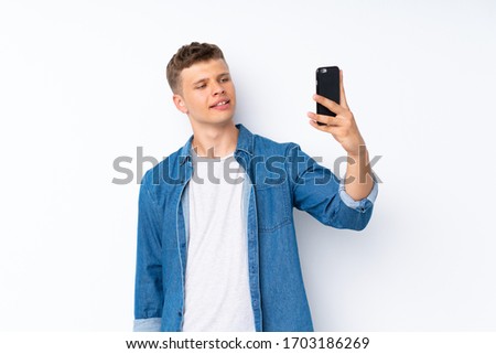 Young handsome man over isolated white background taking a selfie with the mobile
