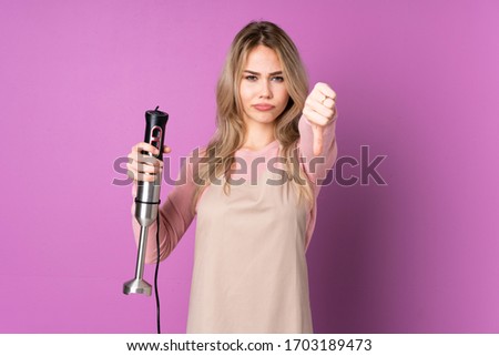 Teenager Russian girl using hand blender isolated on purple background showing thumb down with negative expression