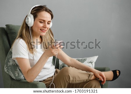 Enjoy the music. Happy young woman pleasing music in white headphones with smartphone. She clothed in white T-shirt and beige pants.