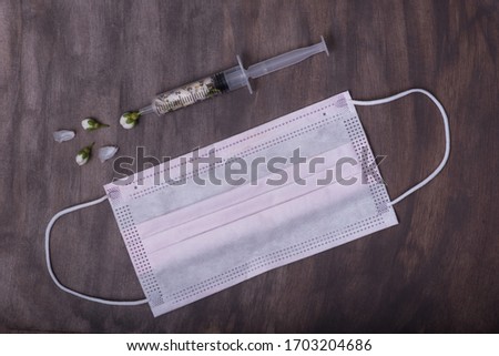  A composition of a medical syringe filled with cherry flowers and a protective mask on a dark vintage background.
