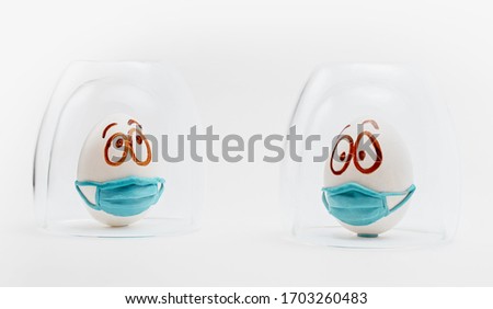 Two easter eggs in medical masks are isolated under glass caps on a white background. The concept of Easter holiday 2020 in connection with the corona virus quarantine and self isolation