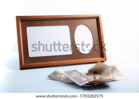 an empty wooden photo frame and mat with a pile of old photos on a blue table