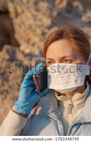 Masked redhead girl phoning in light clothes on the street on a sunny day, protective pandemic