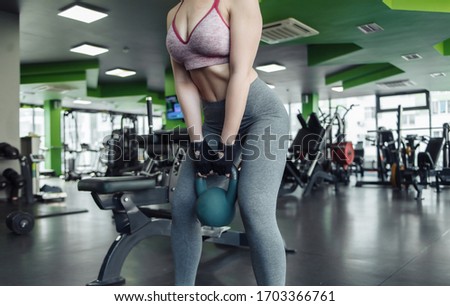 Fit woman in sportswear holds heavy kettlebell in her hands at gym.