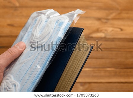 hand with pack of medical masks and a book