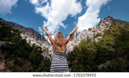 Happy blonde girl faceless look at mountain with hands up. Lifestyle, freedom, mental health concept. Stock photo.