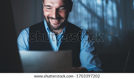 bearded businessman looking paper document at home workplaceat night, smile man working in monitor computer at social distance, online communication work process, online education