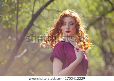 red-haired girl in a burgundy dress walks in the forest