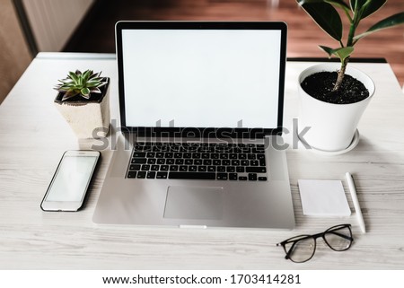 Mockup laptop computer with blank white screen, smartphone, pen, notes, glasses on table. Home interior, office background. Front top view desktop, workplace. Technology concept. copy space.