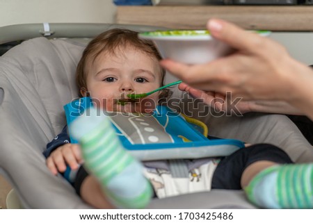 mother feeding her adorable baby boy with a spoon
