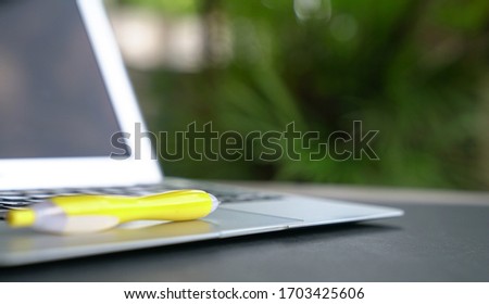 Yellow pen on top of computer laptop with green nature background. Copy space.
