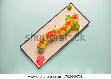Green dragon sushi roll with eel, avocado, cucumber, wasabi sauce and ginger. Sushi rolls philadelphia or california served on a traditional white rectangular plate over blue mint background.