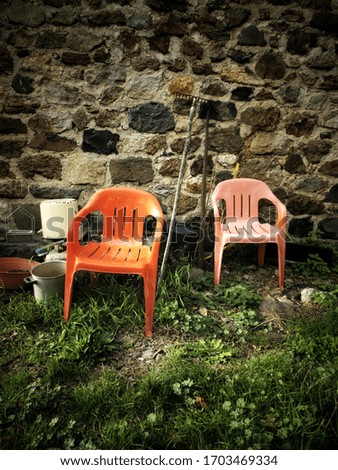 A vertical picture of two plastic chairs on the ground against a wall in a garden