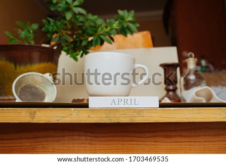 the inscription April on the background of the workplace at home during the period of quarantine and isolation. White Cup on a natural stand made of gray stone with a home green plant