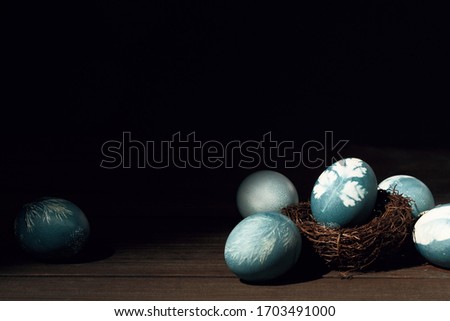 Painted blue eggs with printed picture of parsley in nest on wooden table. Easter decoration concept. Top view rustic background