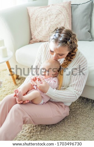 A beautiful young mother holds in her arms a small pretty blue-eyed 2-month-old daughter. Newborn. Baby.