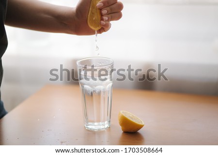 Female hand squeeze lemon juice in glass with water. Water with lemon. Fresh drink on quarantine Royalty-Free Stock Photo #1703508664