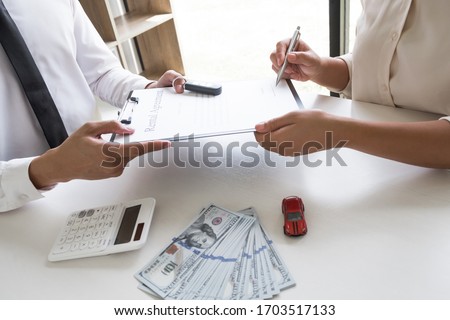 Customer is signing the car rental agreement and getting a car key from dealer after signed in the office, Car rental concept.