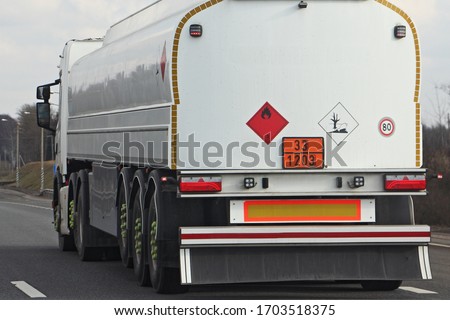White semi truck fuel tanker with 33/1203 dangerous class sign and copy space place blank on barrel drive on asphalt highway on a spring day on blue sky background, side rear view ADR hazardous cargo Royalty-Free Stock Photo #1703518375