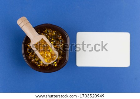 Cod liver oil omega 3 gel capsules with wooden spoon on blue paper background