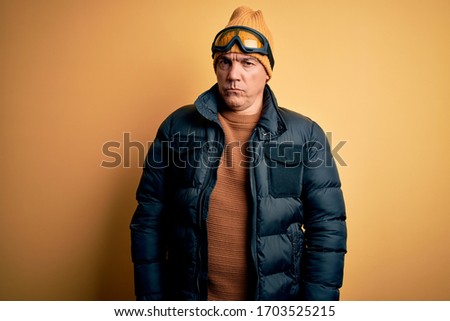 Middle age handsome grey-haired skier man on vacation wearing ski goggles skeptic and nervous, frowning upset because of problem. Negative person.