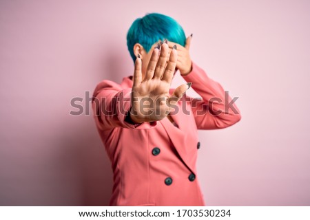 Young beautiful businesswoman with blue fashion hair wearing jacket over pink background covering eyes with hands and doing stop gesture with sad and fear expression. Embarrassed and negative concept.
