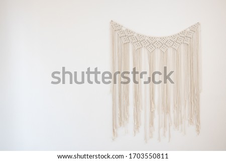 A macrame the art of knotting cord or string in patterns hanging on white cement wall for home and wedding decoration with copy space Royalty-Free Stock Photo #1703550811