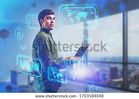 Inspired young businessman using laptop in blurry office with double exposure of futuristic HUD business interface. Concept of technology and internet. Toned image