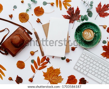 Top view of coffee cup, keyboard and blank paper with autumn leaves. Home workspace, fall scene 