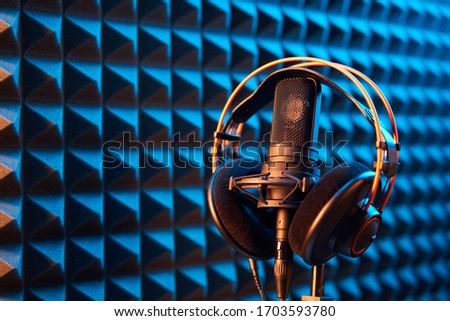 Studio condenser microphone with professional headphones on blue acoustic foam panel background