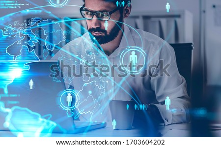 Bearded businessman using laptop in blurry office with double exposure of blurry social network interface. Concept of HR and recruitment. Toned image Royalty-Free Stock Photo #1703604202
