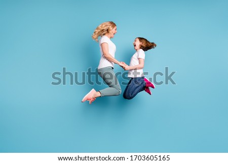 Full length profile photo of funny mom lady little daughter spend time together jumping high up hold hands rejoicing wear casual white s-shirts isolated blue color background