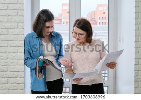 Two women designer and customer working choosing fabrics for curtains, furniture upholstery. Looking different models of curtains, colors on sketches