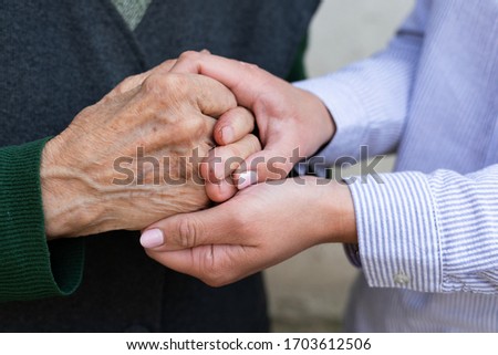 Close up picture of caregiver holding senior woman's wrinkled hands 