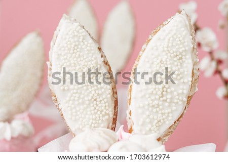 Baked Easter Cookies in Bunny Ears Form Close-up Photo. Beautiful Religious Holiday Cooked Pastry Dessert with White Chocolate and Meringues. Sugary Cakes and Apricot Branch on Blurred Background
