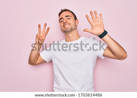 Handsome man with blue eyes wearing casual white t-shirt standing over pink background showing and pointing up with fingers number eight while smiling confident and happy.