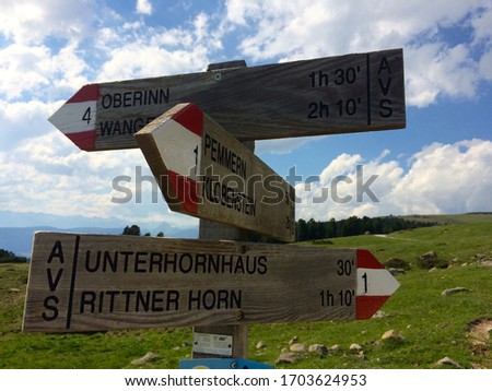 Rustic wooden mountainside three way sign, with a view. Distant mountains, vibrant blue sky, rocky green grass and lush pine forest.
