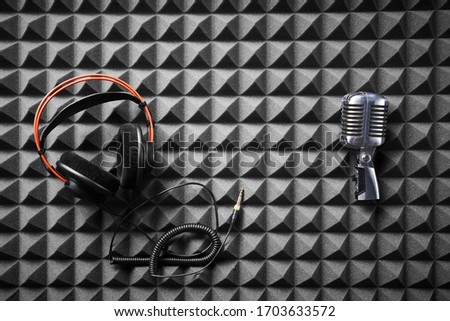 Retro microphone and professional headphones lying on acoustic foam panel background, flat lay