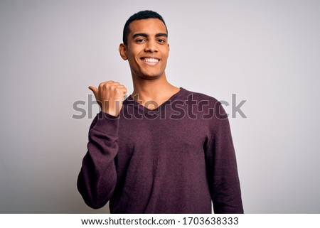 Young handsome african american man wearing casual sweater over white background smiling with happy face looking and pointing to the side with thumb up.