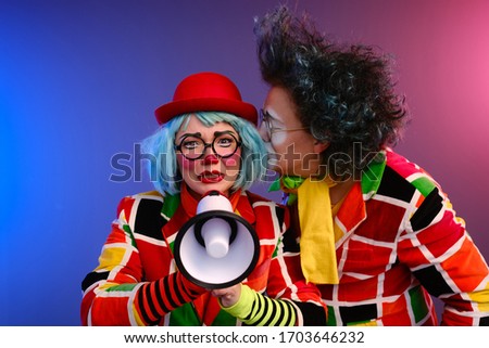 Two clowns a man and a woman with bright makeup in colored costumes speak in a megaphone to make an announcement. April Fools Day concept. Birthday for kids