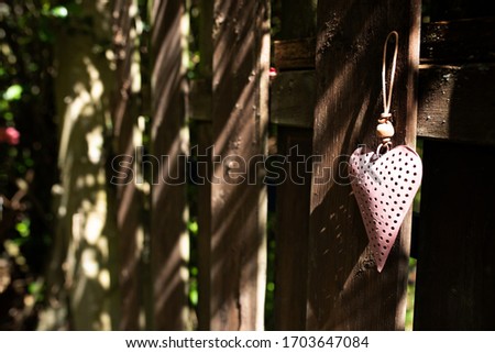 Pink heart at a old wooden fence. Sunny background with short deep of field for a mothers day concept. Space for text.
